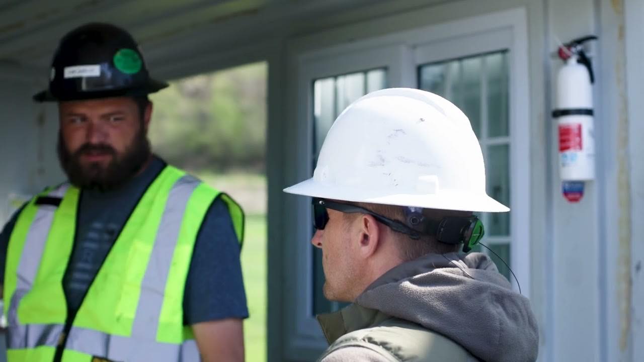 Two Bristola crew members in hard hats and high-visibility vests talking outside a facility building